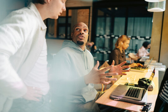 Businessman gesturing while explaining data to male coworker at desk in coworking space