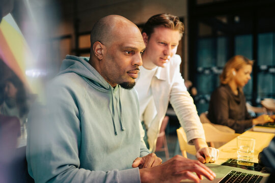 Focused male entrepreneurs reviewing information on laptop in busy office