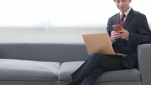 オフィスでノートパソコンとスマホを使う男性ビジネスパーソン