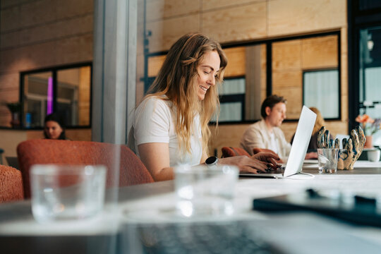 Smiling businesswoman typing mail while working on laptop at shared desk in coworking space