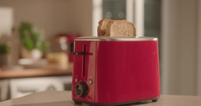 Two slices of toast popping out of a red toaster in a modern kitchen