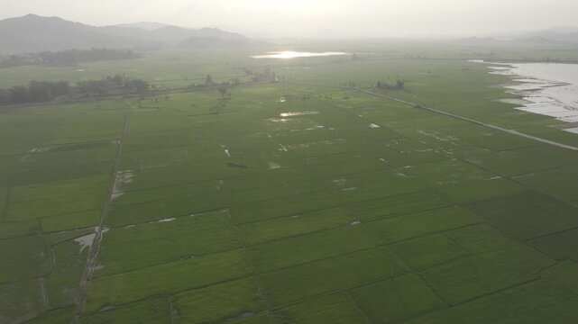 Sunset over Lak Lake in Lien Son Lak Commune, Dak Lak Province, Vietnam, featuring traditional wooden boats on the lake and peaceful rice fields surrounded by the Central Highlands landscape.