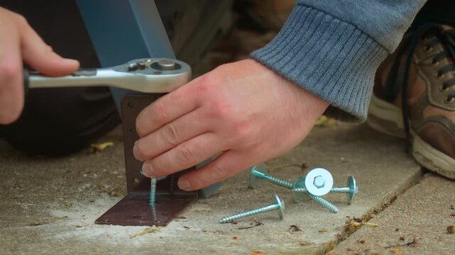 Heavy duty screw driving into dowel inside concrete slab during equipment installation. Hand tool operating ratchet mechanism for tightening fastener on steel bracket base. Building process