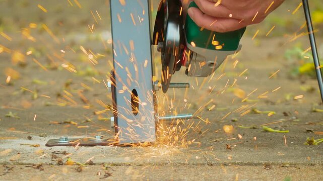 Rotating cutting disc grinding steel bolt head near anchored bracket on concrete base detail. Bright sparks scattering during trimming operation in structural mounting workflow. Industrial