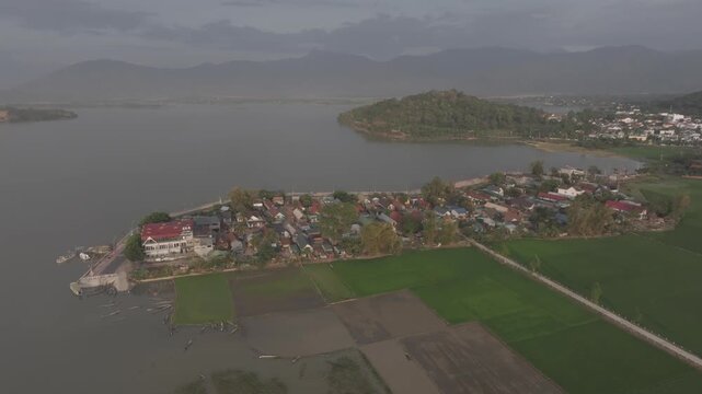 Sunset over Lak Lake in Lien Son Lak Commune, Dak Lak Province, Vietnam, featuring traditional wooden boats on the lake and peaceful rice fields surrounded by the Central Highlands landscape.
