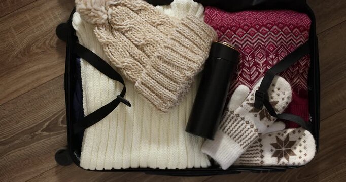 Hand puts thermos in suitcase with winter clothes for travel