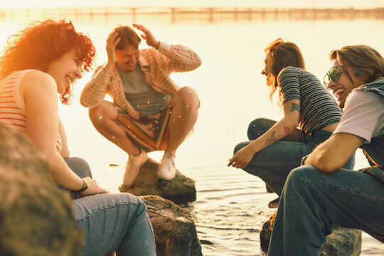 Laughing friends crouching by lakeshore at sunset with nostalgic film grain. Concept of candid youth content, friendship campaigns, summer fun, travel memories, and emotional lifestyle ads.
