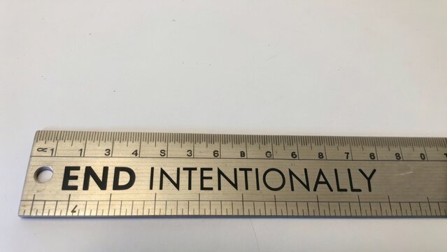 Metal ruler with engraved text stating "END INTENTIONALLY" on a white background, showcasing measurement and precision in design