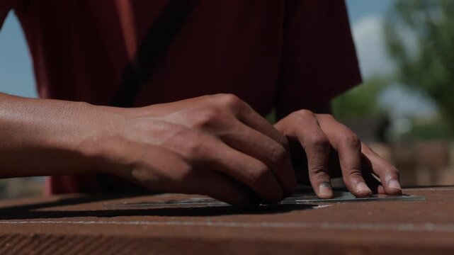 Macro detail of a master craftsman drawing precise lines on a volcanic stone surface with a ruler for traditional carving under sunlight.