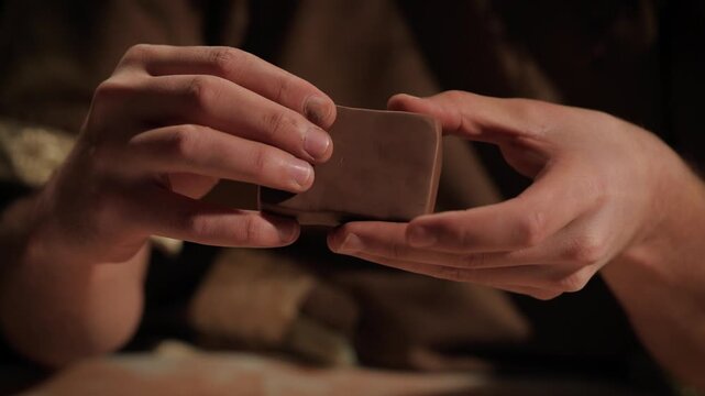 Macro shot of a clay tablet ready to be engraved, held by a person's hands.