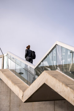 A person climbs stairs beside glass railing on a concrete bridge in Oslo, Norway Barcode, set against pale sky and angular lines above the street
