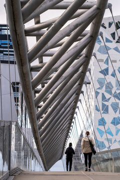 pedestrians walk beneath the steel truss of Akrobaten bridge in Oslo, Norway Barcode, with the facade pattern closing the walkway ahead