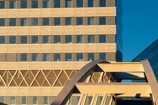 Low sunlight reaches a patterned office facade in Stockholm, Sweden, where windows sit behind an arch bridge and strong geometry above the street