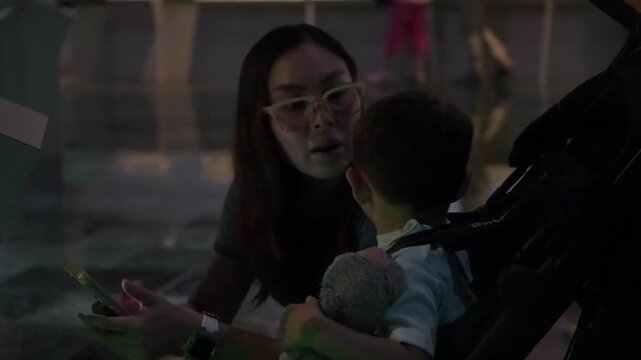 A young Latina mother and her baby are closely examining a museum exhibit. They use a cell phone to scan a QR code for information, demonstrating engagement in learning and discovery.