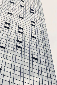 A white skyscraper facade extends upward in strong perspective, where grid windows and small dark openings shape the tower pattern against urban height