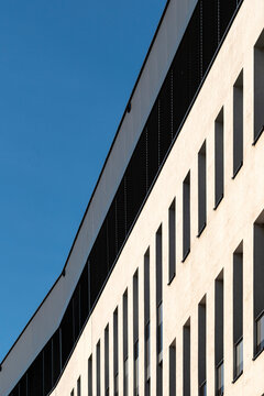 A curved beige office facade rises under blue sky, where windows, shadow and clean lines turn the building edge into layered urban geometry