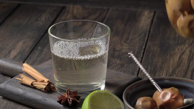 Wild pear beverage pouring from jar into glass on wooden surface with fruit and spices nearby.