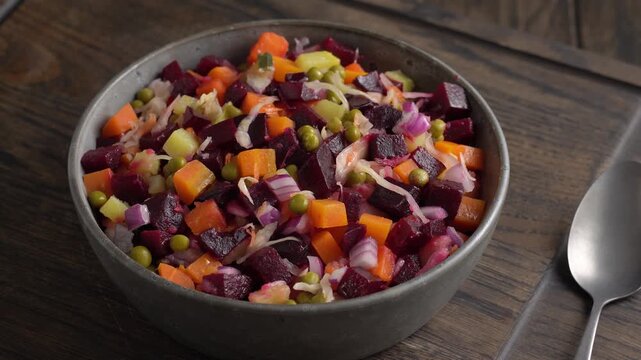 Bowl of Russian vinaigrette salad sits on wooden table rotating.