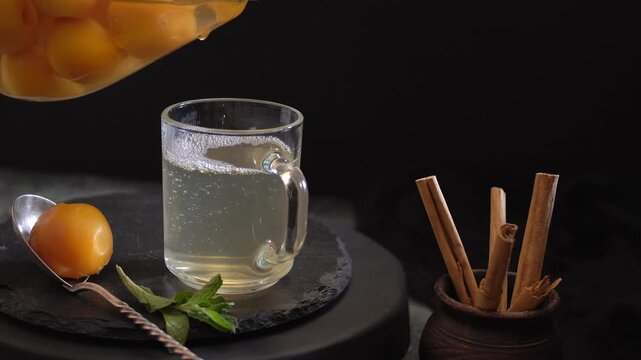 Apricot drink is pouring from jar into glass with cinnamon sticks nearby.