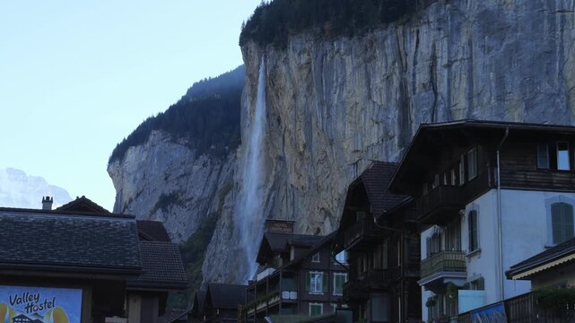 Majestic Staubbach Falls cascading down a towering cliff behind charming wooden chalets in the alpine village of Lauterbrunnen, Switzerland