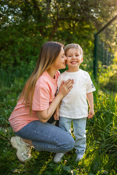Mother kneeling and kissing her smiling young son in a sunny outdoor family moment