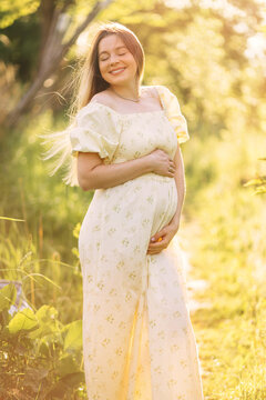 Pregnant woman in a floral maternity dress smiling in golden hour sunlight outdoors