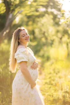 Pregnant woman in a floral maternity dress enjoying golden hour sunlight in a peaceful summer meadow
