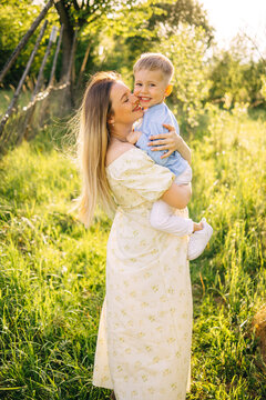 Mother holding smiling son in sunlit meadow &mdash; family love and summer outdoor portrait