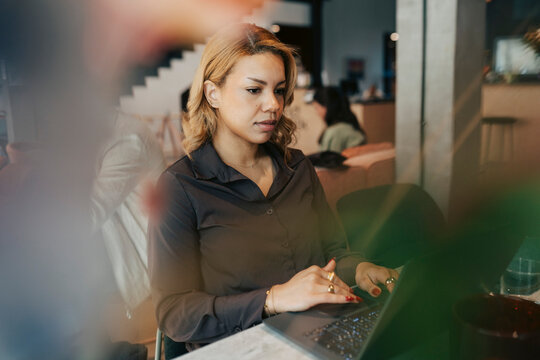 Focused businesswoman preparing reports on laptop while sitting and working at shared coworking space