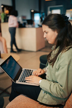 Businesswoman working on laptop while sitting on couch at coworking space