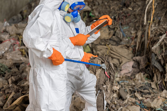 Hazardous Waste Management:Two specialists in a full hazmat suit,respirator examines environmental samples amidst a large pile of refuse, highlighting critical hazardous waste management and safety.