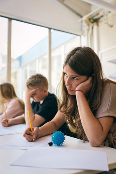 Contemplative teenage girl with ADD sitting for educational exam with stress ball in junior high school