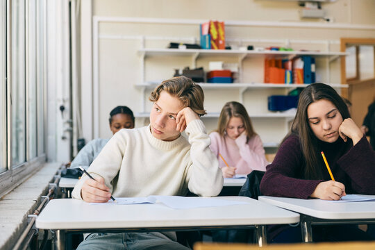 Contemplative teenage boy sitting for educational exam in classroom at school