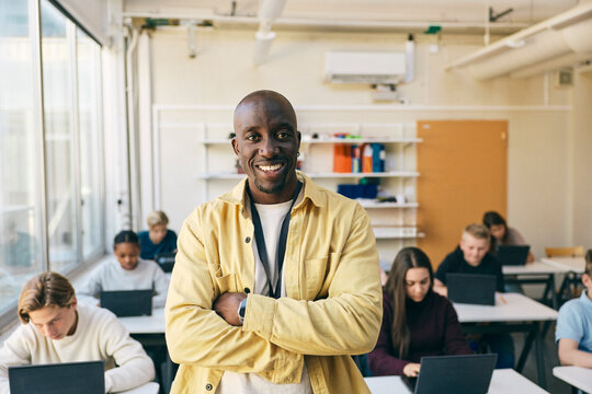 Portrait of smiling teacher standing with arms crossed in classroom at junior high school