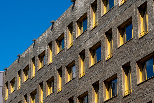 Stone apartment facade in La Confluence, Lyon, France angles under blue sky, where yellow windows and pattern create strong residential geometry