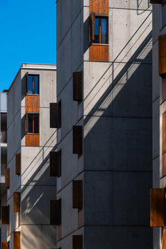 In La Confluence, Lyon, France, concrete apartment facade shadows fall across wood windows, creating vertical rhythm on the residential block