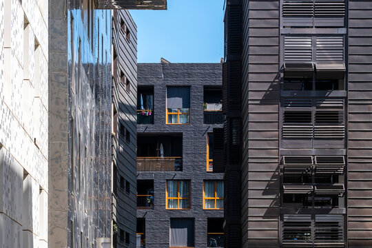 Reflective apartment facades in La Confluence, Lyon, France face each other across a courtyard, with windows and shadow layering residential depth