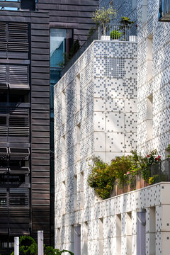 In La Confluence, Lyon, France, a white apartment facade with perforated pattern and plants faces a dark building across the urban courtyard