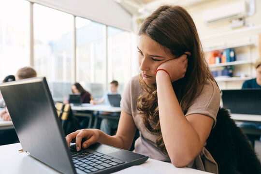 Teenage girl leaning on elbow while using laptop in classroom at school
