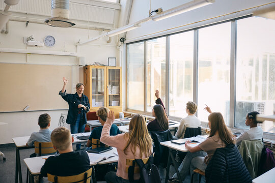 High angle view of students raising hand with teacher in classroom at junior high school