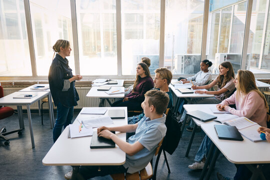 Smiling female professor talking with students while teaching in classroom at school