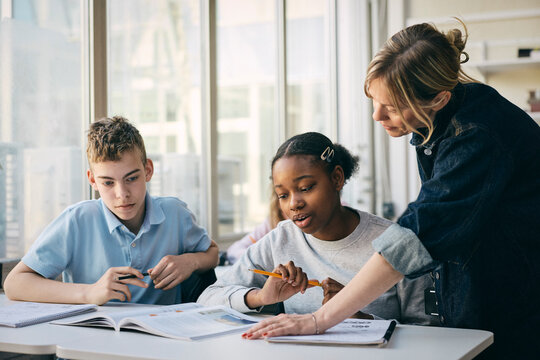 Female professor guiding students with studies in classroom at junior high school