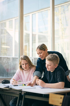 Female teacher guiding students with studies in classroom at junior high school