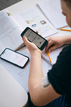 Over the shoulder view of boy checking blood sugar level while sitting at desk with books in classroom