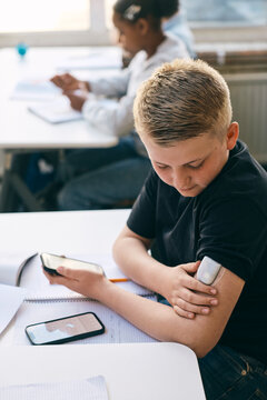 Junior high student checking blood sugar level through glucose meter while sitting at desk with books in classroom