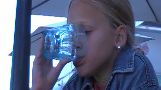 girl drinking water outdoors in summer retro style filmed on analog vhs camera with vintage denim jacket and pink scrunchie
