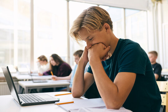 Teenage male student leaning on elbows while studying in classroom at school