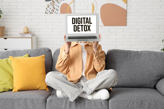 Young woman on sofa holding modern laptop with blank screen at home