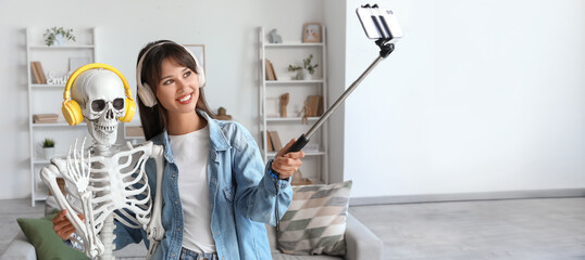 Young woman with human skeleton model in headphones taking selfie at home