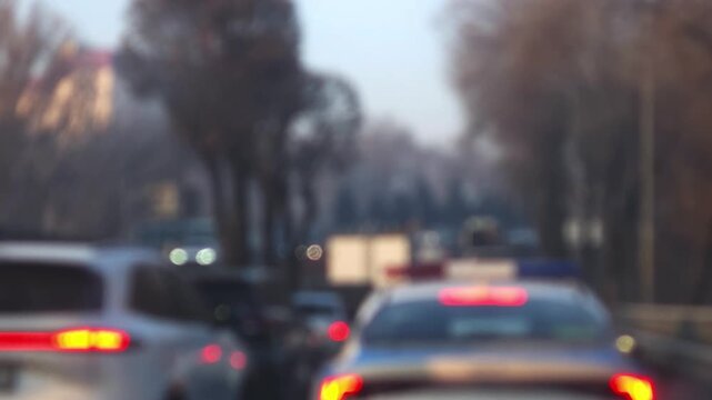 blurred bokeh video of a city street traffic jam in the evening with flashing blue and red lights of a police patrol car